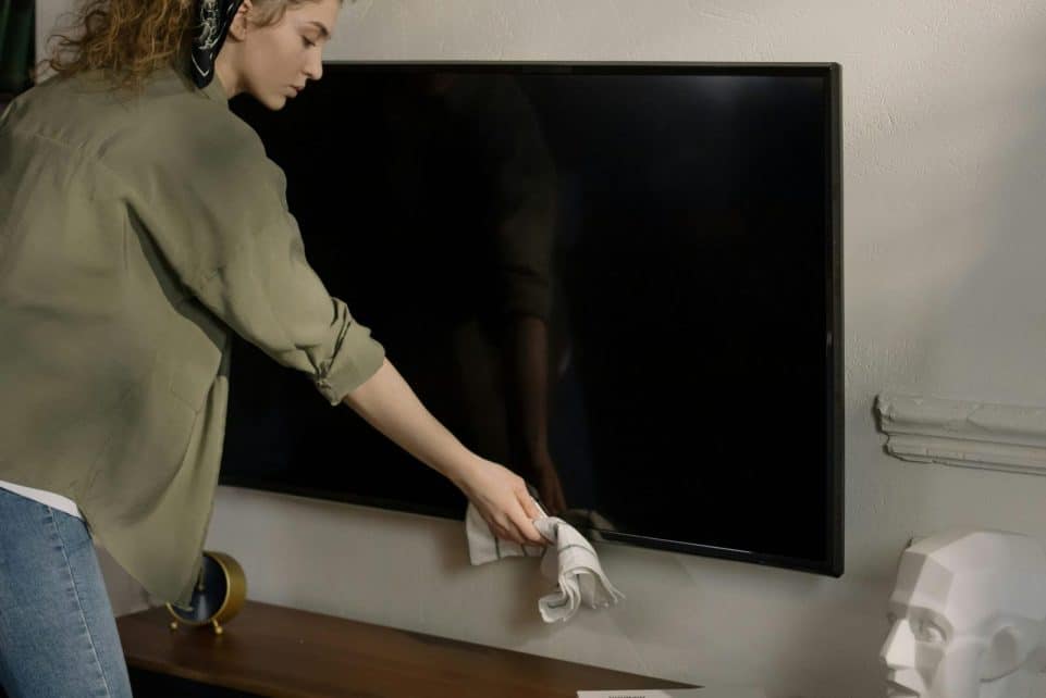 A woman cleaning a black screen TV in a cozy home environment, promoting cleanliness.