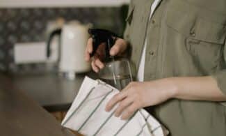 A person cleaning a kitchen counter with a spray bottle and cloth, maintaining cleanliness.