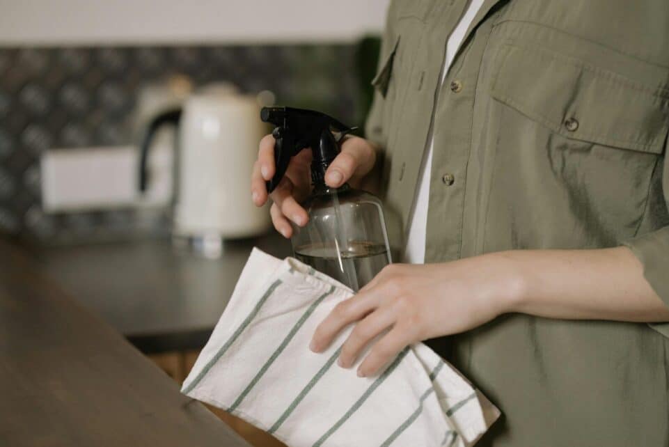 A person cleaning a kitchen counter with a spray bottle and cloth, maintaining cleanliness.