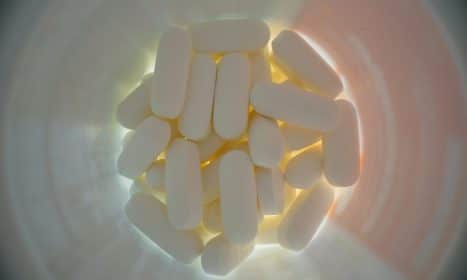 Top view of plastic jar filled with white medical pill in soft light