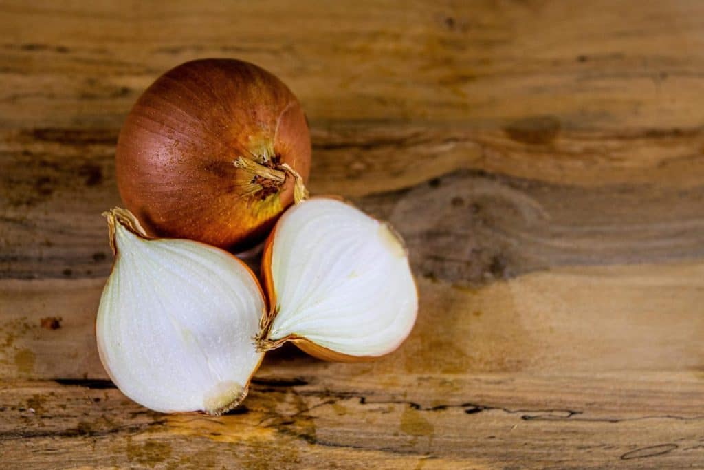 Detailed view of a whole and sliced onion on a textured wooden surface.
