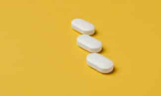 Three white pills on a vibrant yellow background, conveying healthcare and medication themes.