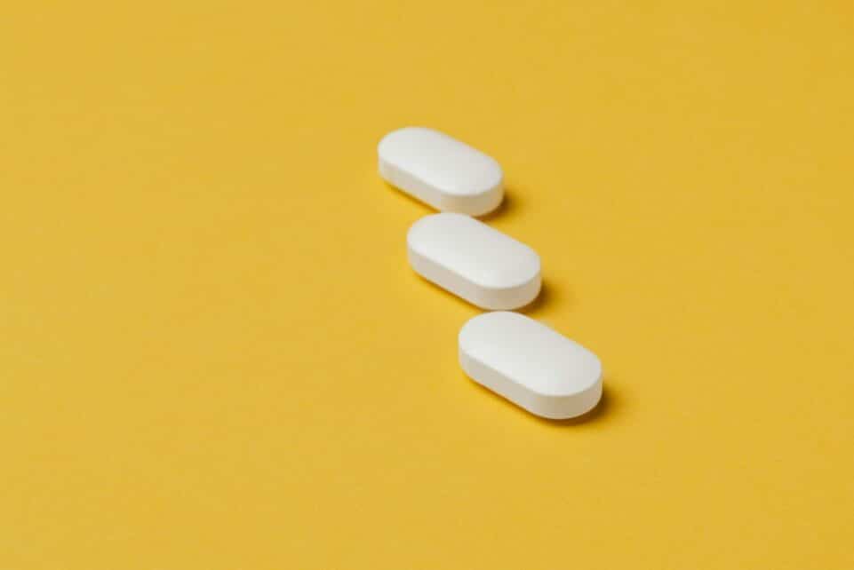 Three white pills on a vibrant yellow background, conveying healthcare and medication themes.