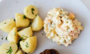 A delectable plate of potato salad with herbs, served alongside boiled potatoes and a meatball, perfect for dinner.