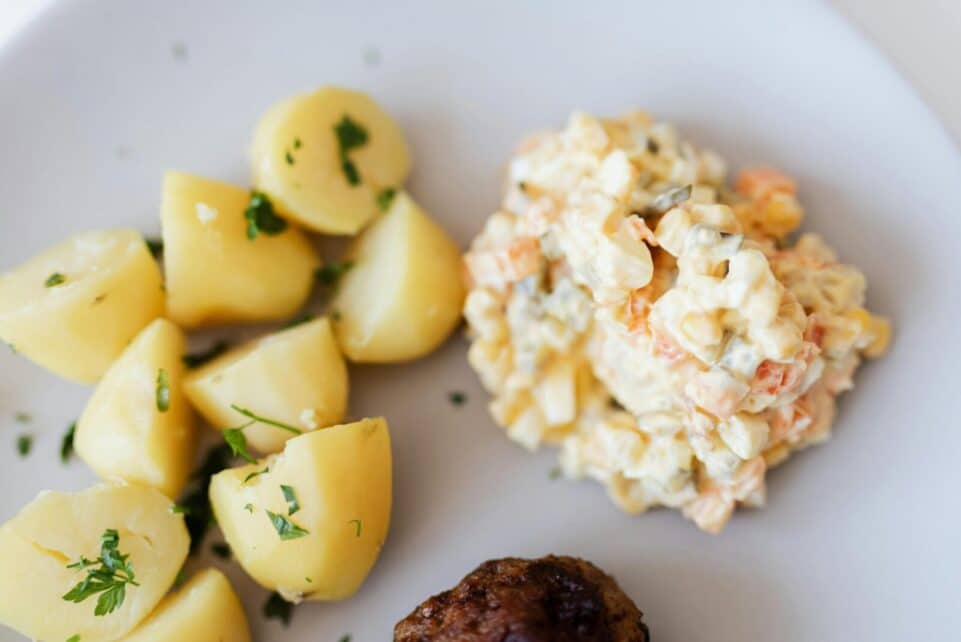 A delectable plate of potato salad with herbs, served alongside boiled potatoes and a meatball, perfect for dinner.