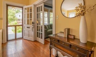 Sunlit entryway featuring a wooden dresser, mirror, and vase with decorative branches.