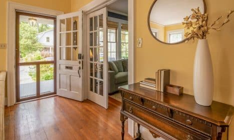 Sunlit entryway featuring a wooden dresser, mirror, and vase with decorative branches.