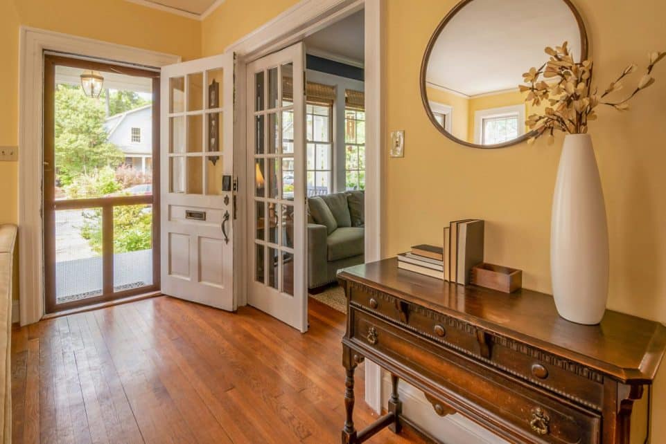 Sunlit entryway featuring a wooden dresser, mirror, and vase with decorative branches.