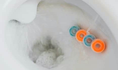 From above of flushing water in toilet bowl with cleaner and freshener block