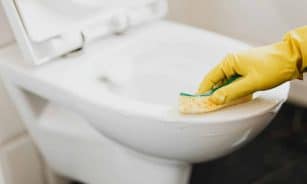 Close-up of a gloved hand using a sponge to clean a toilet, focusing on hygiene.