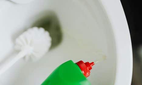 Green bottle pouring cleaner into toilet bowl with a brush beside it, emphasizing bathroom hygiene.