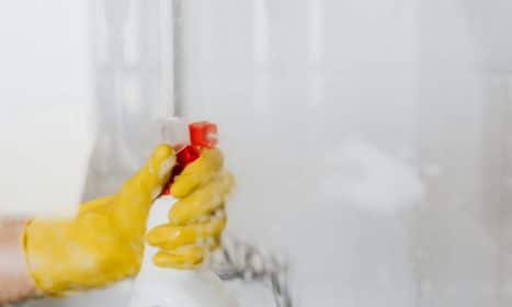 Person wearing yellow gloves cleaning a glass surface with a spray bottle.