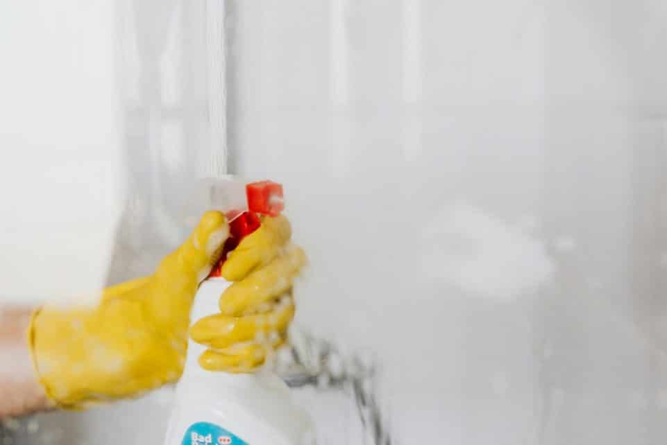 Person wearing yellow gloves cleaning a glass surface with a spray bottle.