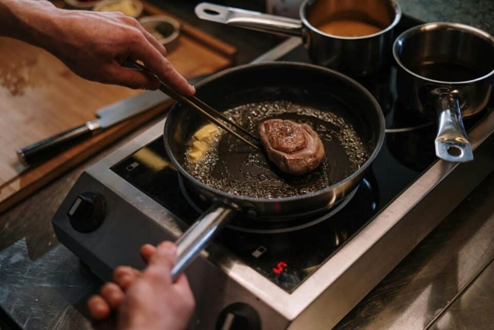 Close-up of pan-seared steak in kitchen stove setting with hands involved, capturing culinary artistry.
