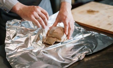 Close-up of a chef's hands wrapping food ingredients in foil for cooking.