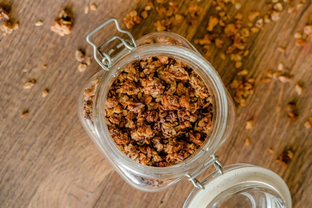 Top view of a glass jar filled with crunchy homemade granola on a wooden surface.