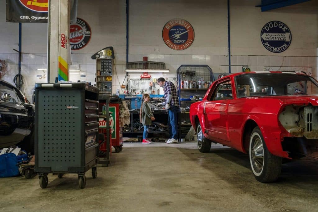 A father and daughter spend quality time together in a bustling auto repair shop, fixing cars.