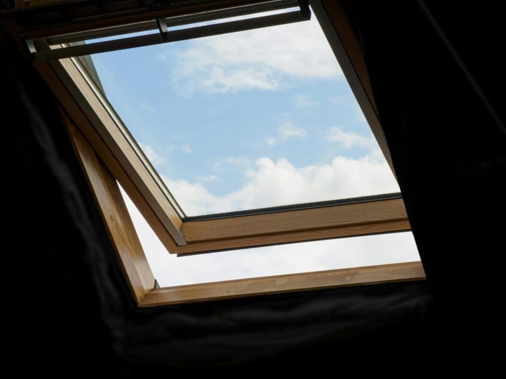 Low angle view of an open skylight with blue sky and white clouds visible.