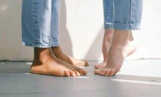 Close-up of an interracial couple standing barefoot on a concrete floor in jeans.