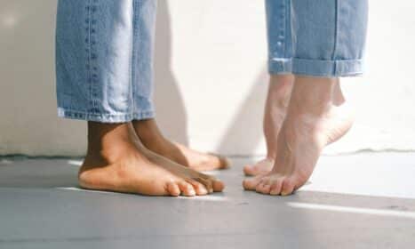 Close-up of an interracial couple standing barefoot on a concrete floor in jeans.