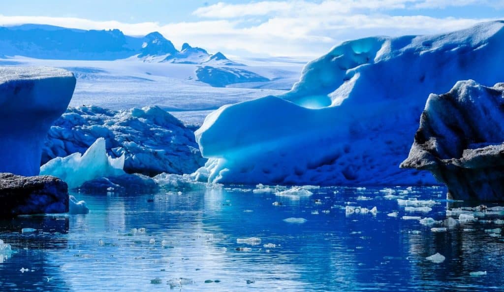 A breathtaking view of glaciers and icebergs reflecting in calm Arctic waters against snowy mountains.