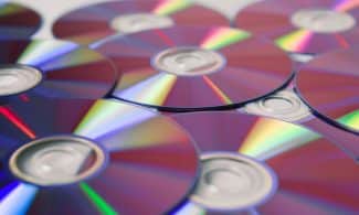 Stack of colorful CDs reflecting light, showcasing vibrant refractions and round patterns.