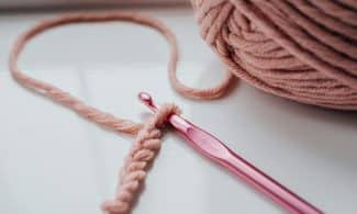 Close-up of pink yarn and crochet hook on a bright indoor windowsill, showcasing a cozy creative hobby.