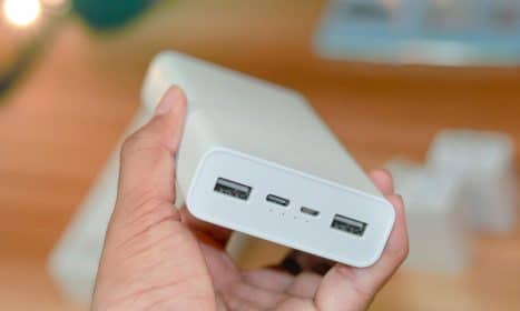 Hand holding a powerbank showcasing its USB ports on a wooden background.