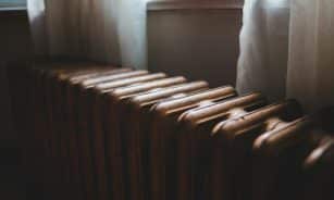 Aged heating battery made of cast iron near windowsill with curtains in house