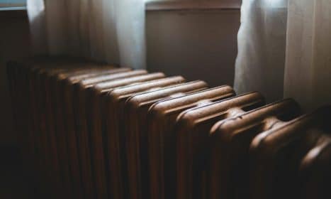 Aged heating battery made of cast iron near windowsill with curtains in house