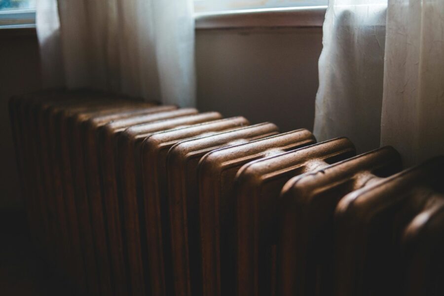 Aged heating battery made of cast iron near windowsill with curtains in house