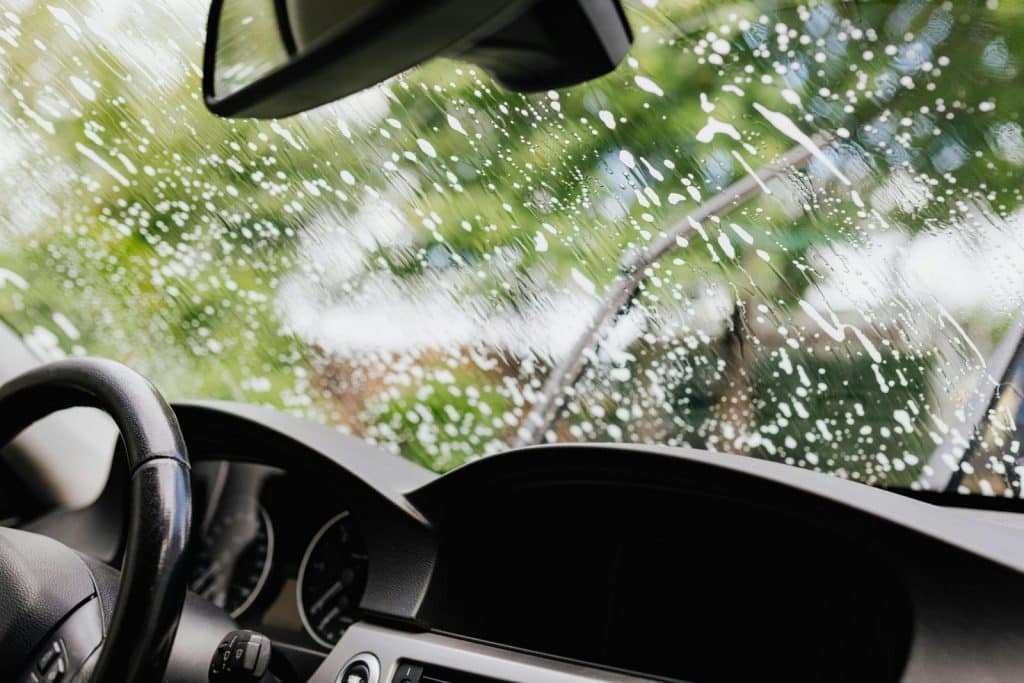 Interior view of a car with soapy windshield during cleaning. Clear dashboard visible.