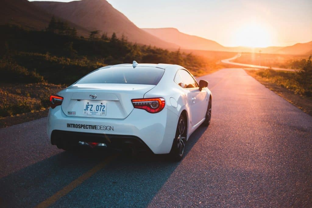 Back bumper of grand tourer car on empty remote route in mountains glowing in sunset