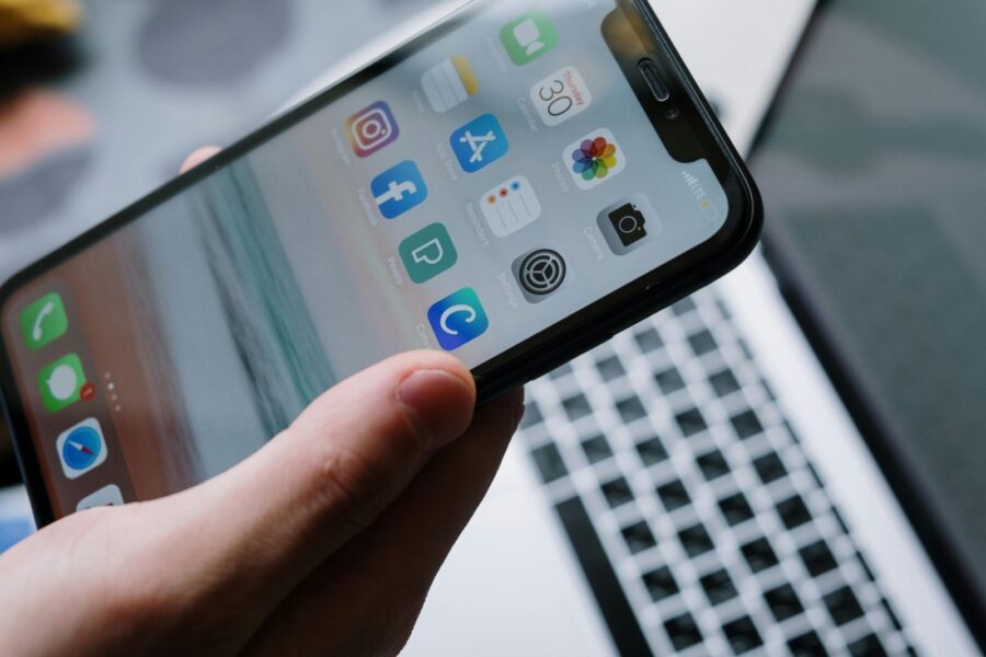 Person holding a smartphone in front of a laptop showcasing various app icons, highlighting digital connectivity.