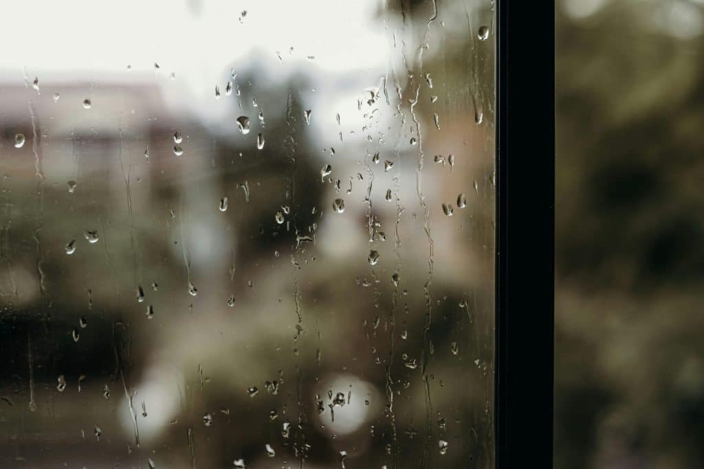 Close-up of raindrops on a window with a blurred view outside, creating a moody atmosphere.
