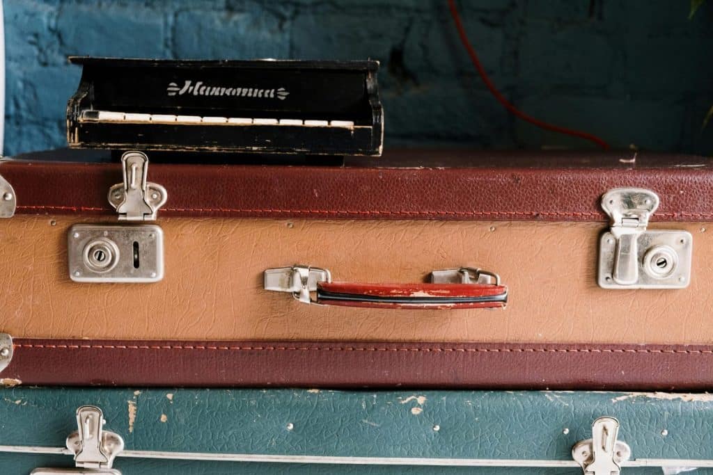 Stack of vintage suitcases topped with an antique harmonium music box against a brick wall.