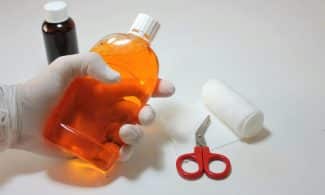 Hand holding orange antiseptic bottle with first aid items, ideal for healthcare themes.