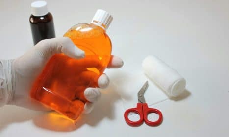 Hand holding orange antiseptic bottle with first aid items, ideal for healthcare themes.