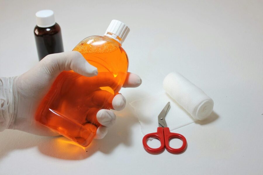Hand holding orange antiseptic bottle with first aid items, ideal for healthcare themes.