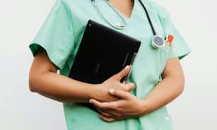 Close-up of a nurse in green scrubs holding a tablet and stethoscope, symbolizing modern healthcare.