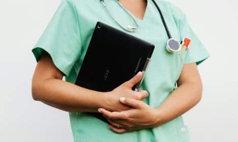Close-up of a nurse in green scrubs holding a tablet and stethoscope, symbolizing modern healthcare.