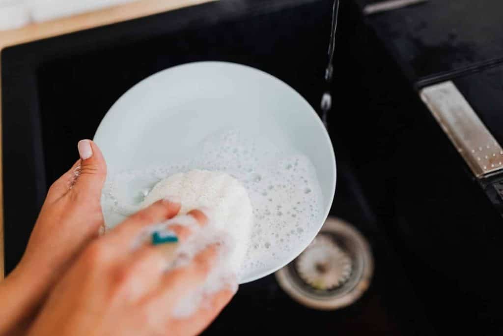 A person washing a plate with soap suds at a kitchen sink, emphasizing cleanliness.