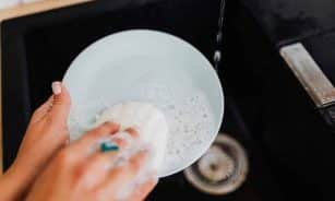 A person washing a plate with soap suds at a kitchen sink, emphasizing cleanliness.