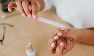 Detailed view of hands filing nails with a nail polish bottle nearby, showcasing personal grooming.