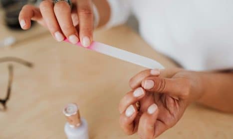 Detailed view of hands filing nails with a nail polish bottle nearby, showcasing personal grooming.