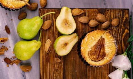 Close-up of a rustic pear tart surrounded by fresh pears and almonds on a wooden board.