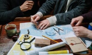 Adults planning a nautical journey using maps, compass, and tools indoors.