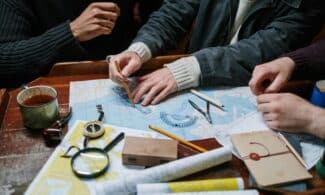 Adults planning a nautical journey using maps, compass, and tools indoors.