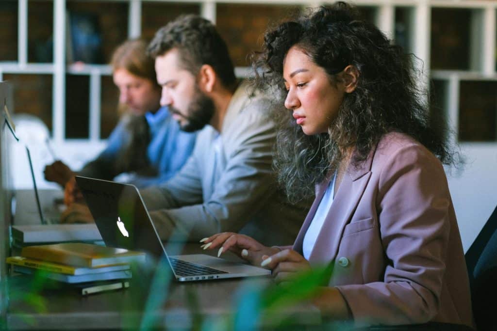 Focused young professionals collaborate on laptops in modern office setting.