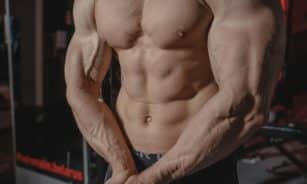 Shirtless male bodybuilder showing muscular torso and defined arms in a gym setting.